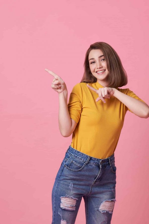 happy-young-woman-standing-with-her-finger-pointing-pink-banner-with-copy-space